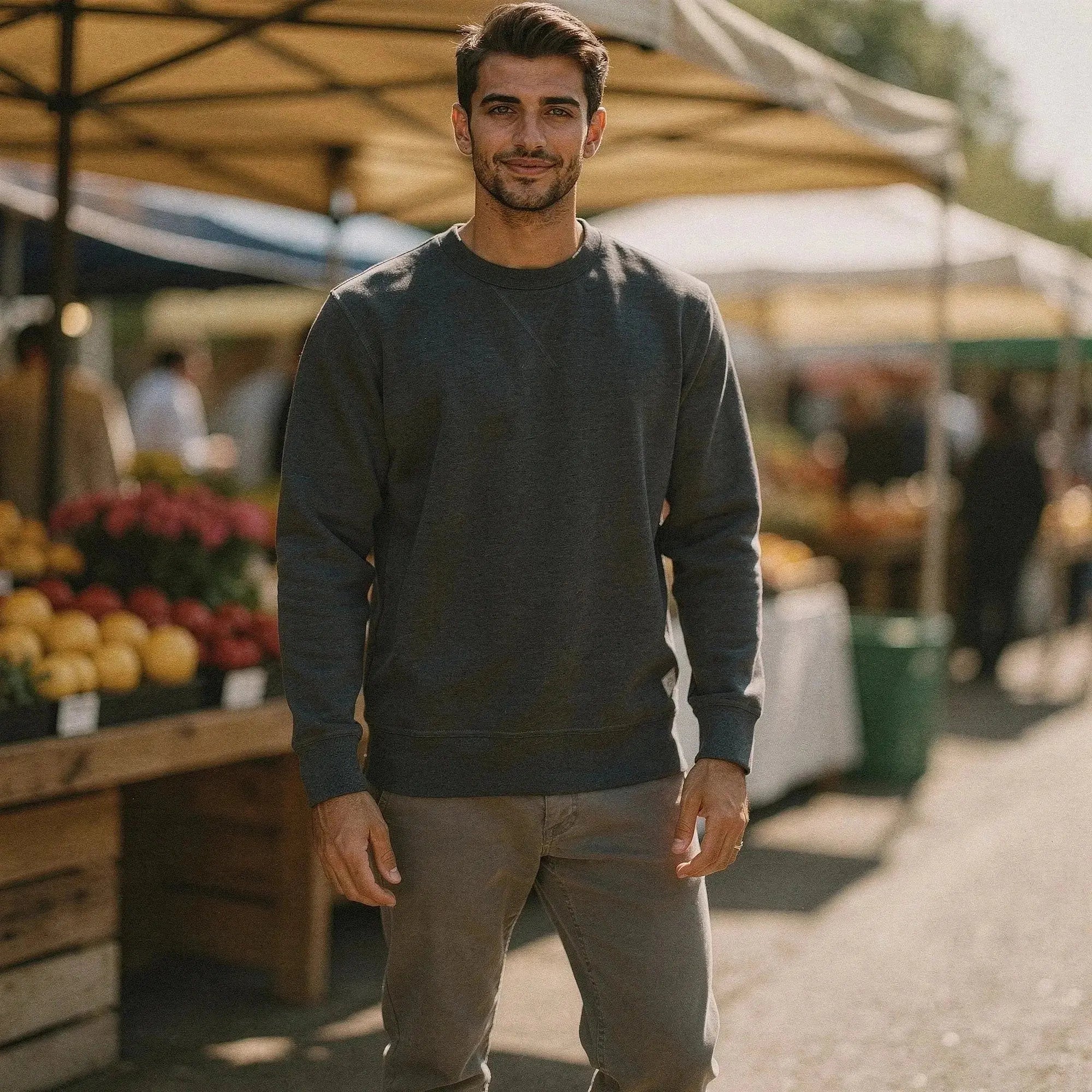 Man wearing a dark gray long sleeve sweatshirt, standing outdoors near market stalls with fruits