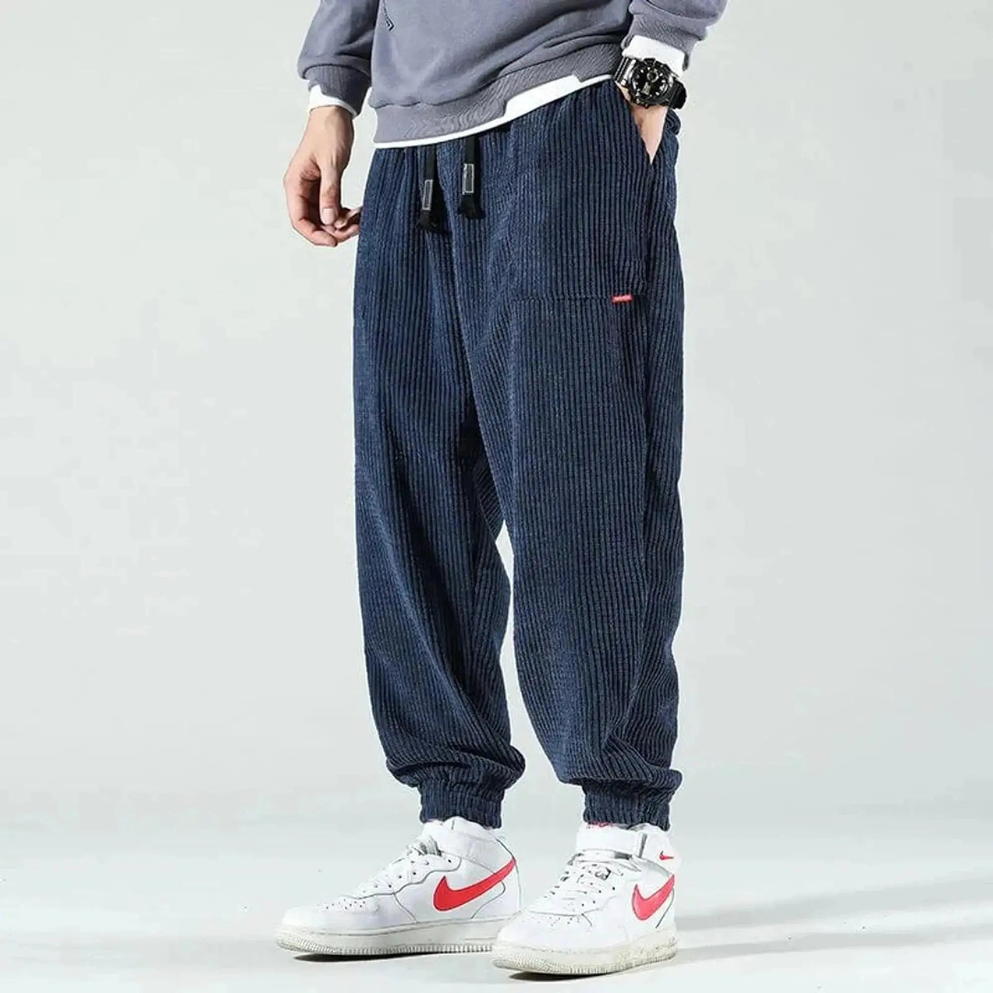 Man wearing navy corduroy joggers with drawstring, standing sideways, hands in pockets, white sneakers