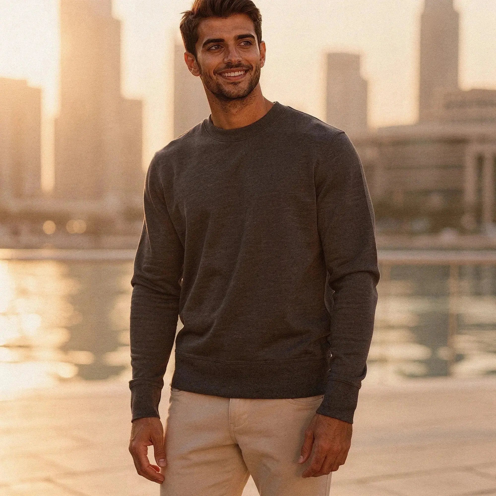 Man wearing a dark gray long sleeve sweatshirt, standing outdoors with city skyline in background