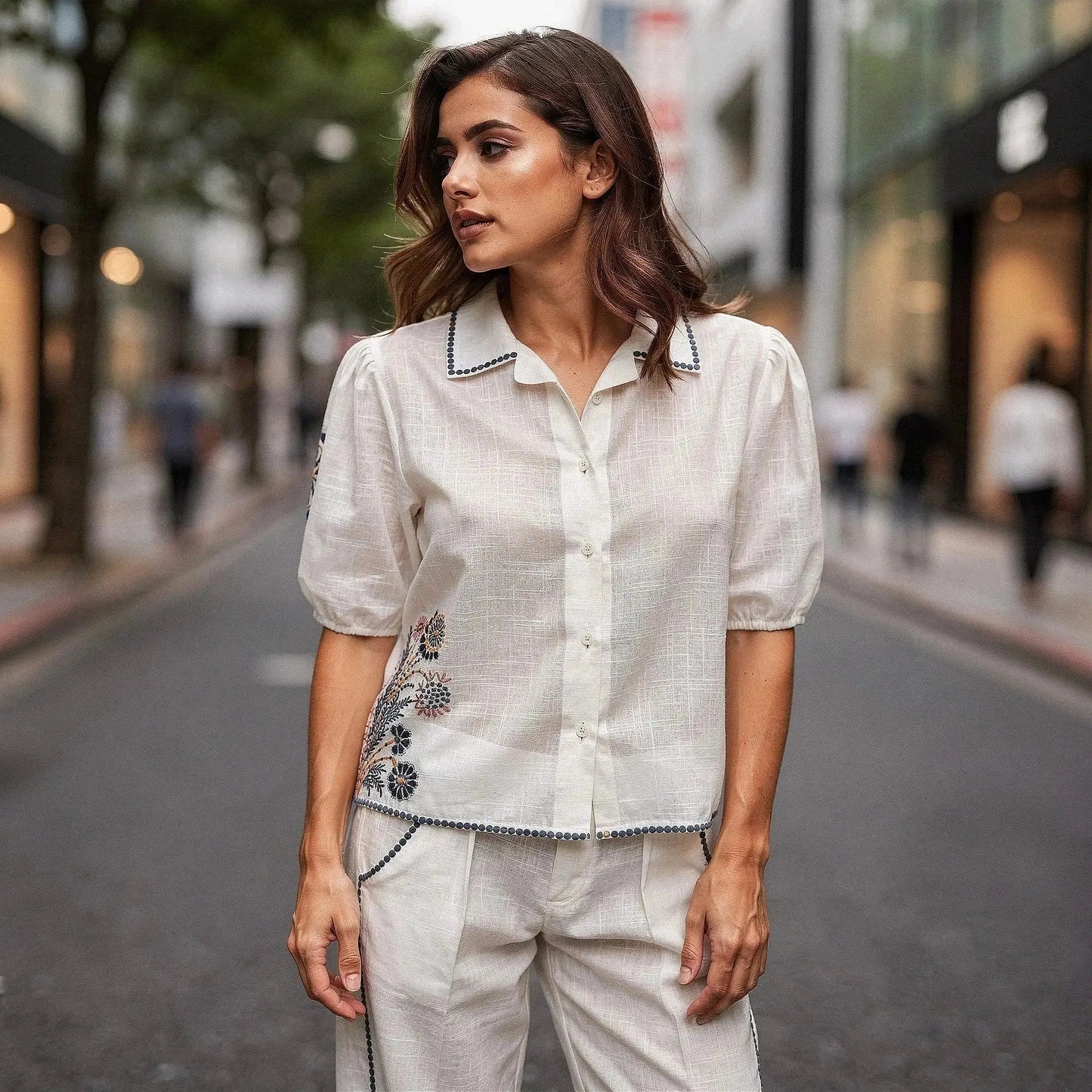 Woman wearing a white short sleeve shirt with floral embroidery, standing on a city street