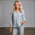 Woman wearing light blue chiffon top with lace trim, standing hands in pockets, against plain backdrop