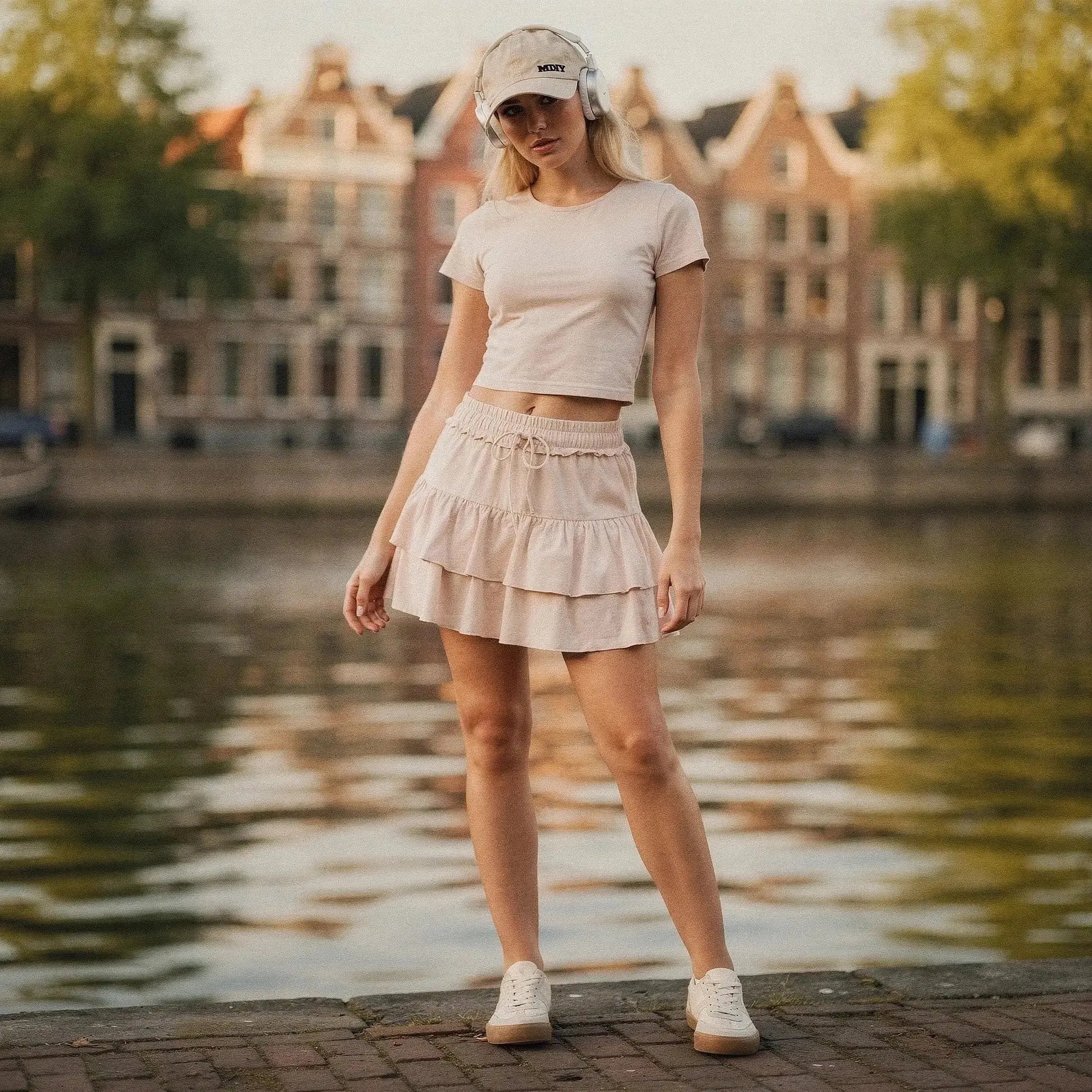Woman wearing beige ruffle mini skirt with shorts, matching crop top, cap, and white sneakers