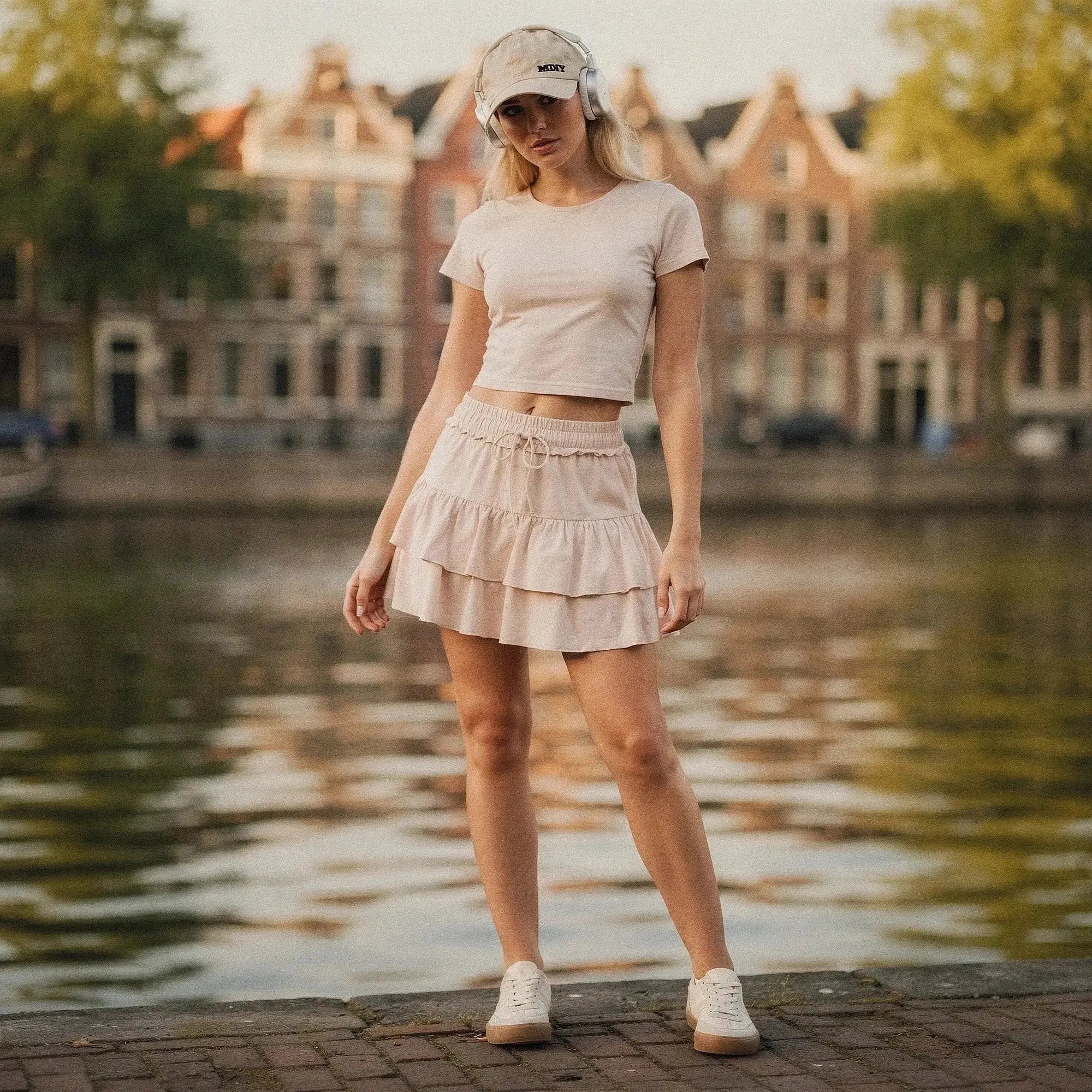 Woman wearing beige ruffle mini skirt with shorts, matching crop top, cap, and white sneakers