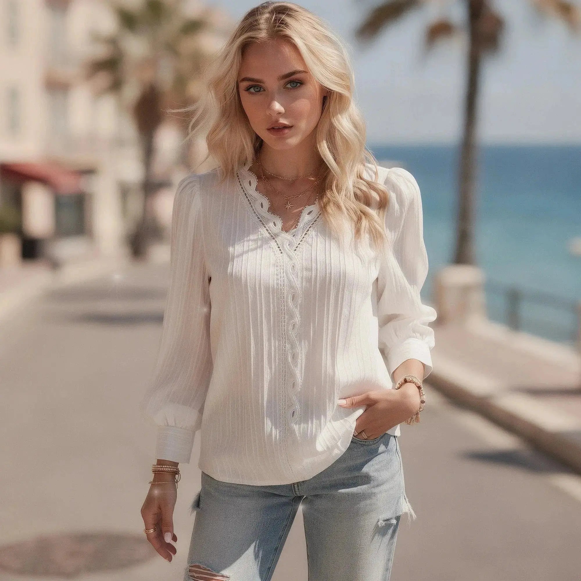Woman wearing a white chiffon top with lace details, standing outdoors near a beachside promenade
