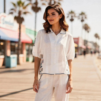 Woman wearing white short sleeve shirt with floral embroidery, standing outdoors on boardwalk