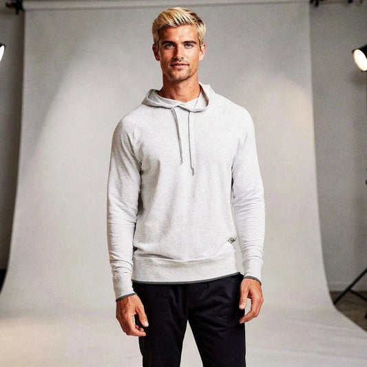 Man wearing a light gray long sleeve hoodie, standing confidently with hands relaxed, against a backdrop