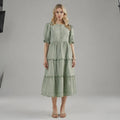 Woman wearing a light green A line midi dress with scalloped hem, standing facing on plain background