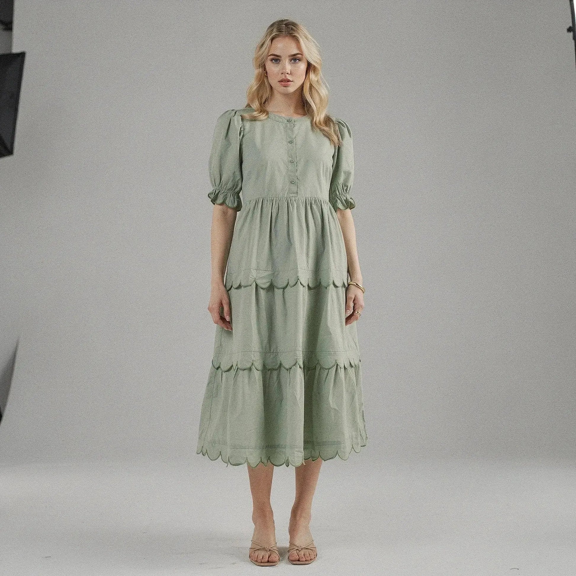 Woman wearing a light green A line midi dress with scalloped hem, standing facing on plain background