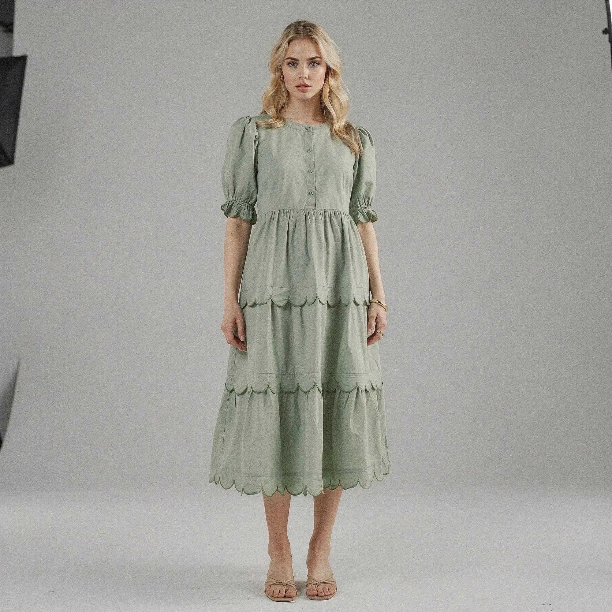 Woman wearing a light green A line midi dress with scalloped hem, standing facing on plain background