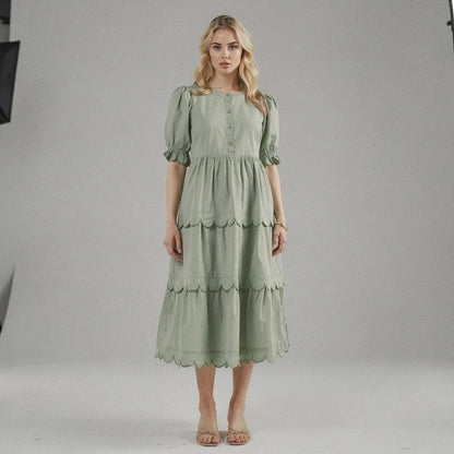 Woman wearing a light green A line midi dress with scalloped hem, standing facing on plain background