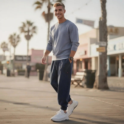 Man wearing navy corduroy joggers and gray sweater, standing outdoors on a sunny boardwalk