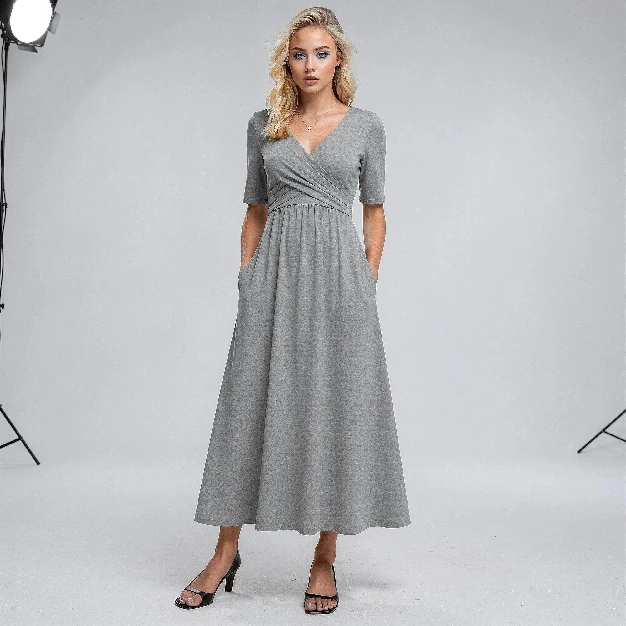Woman wearing a gray midi dress with short sleeves, V neckline, and hands in pockets, standing
