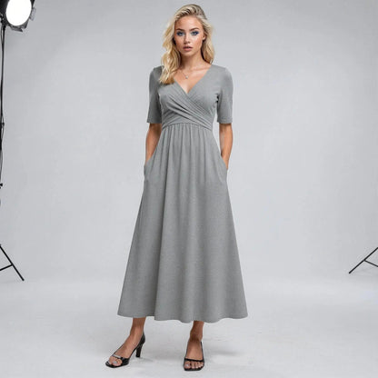 Woman wearing a gray midi dress with short sleeves, V neckline, and hands in pockets, standing