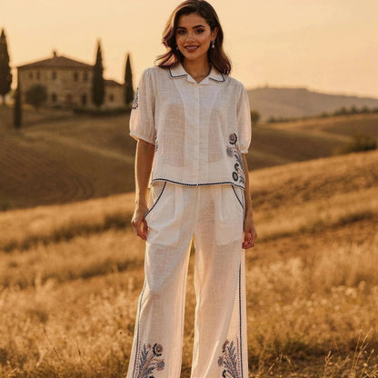 Woman wearing a white short sleeve shirt with blue floral embroidery, standing in a sunlit field