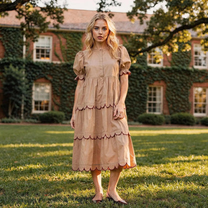 Woman wearing a beige A line midi dress with scalloped hem, standing outdoors on grass