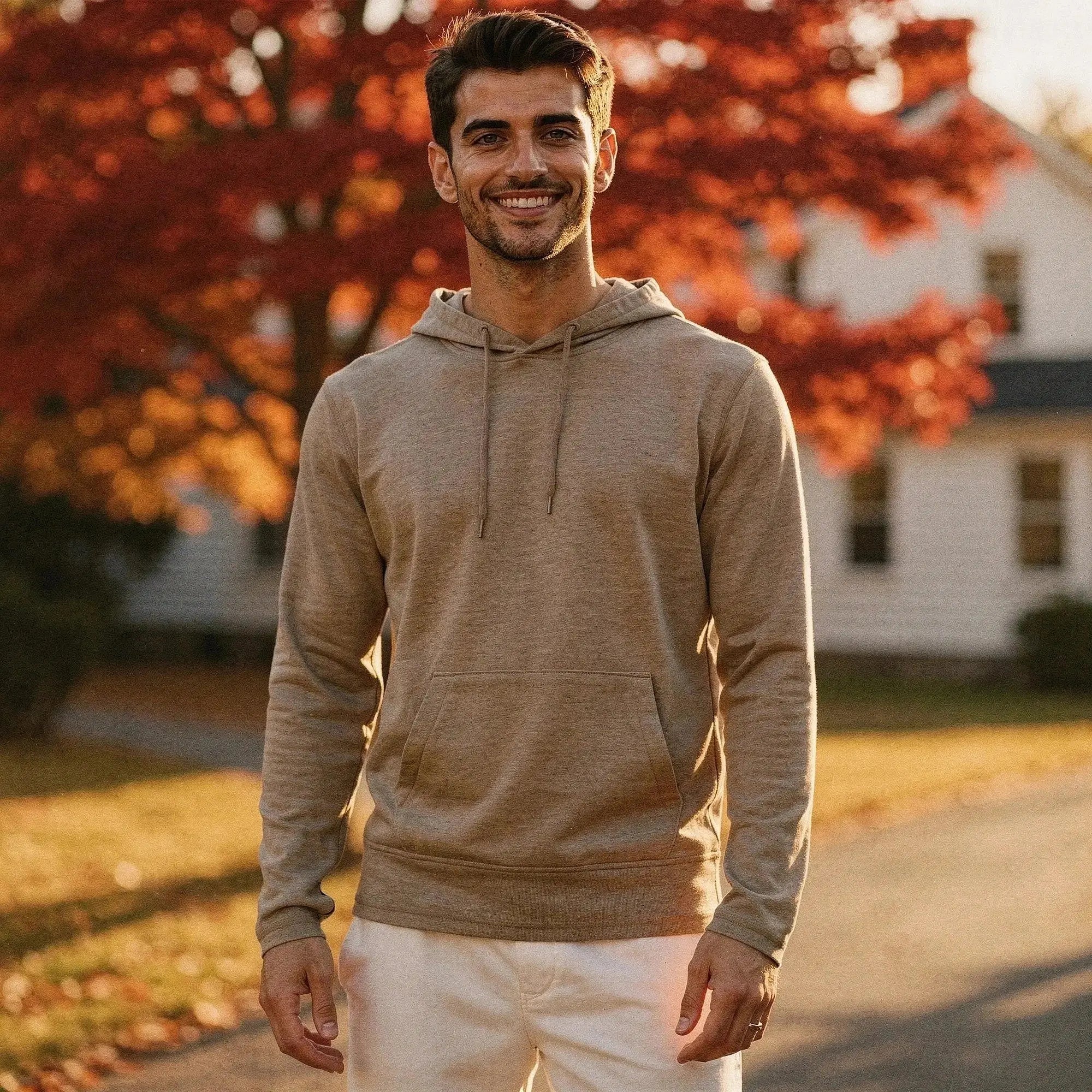 Man wearing a tan slim fit hoodie with drawstrings, standing outdoors, smiling, with autumn trees in background