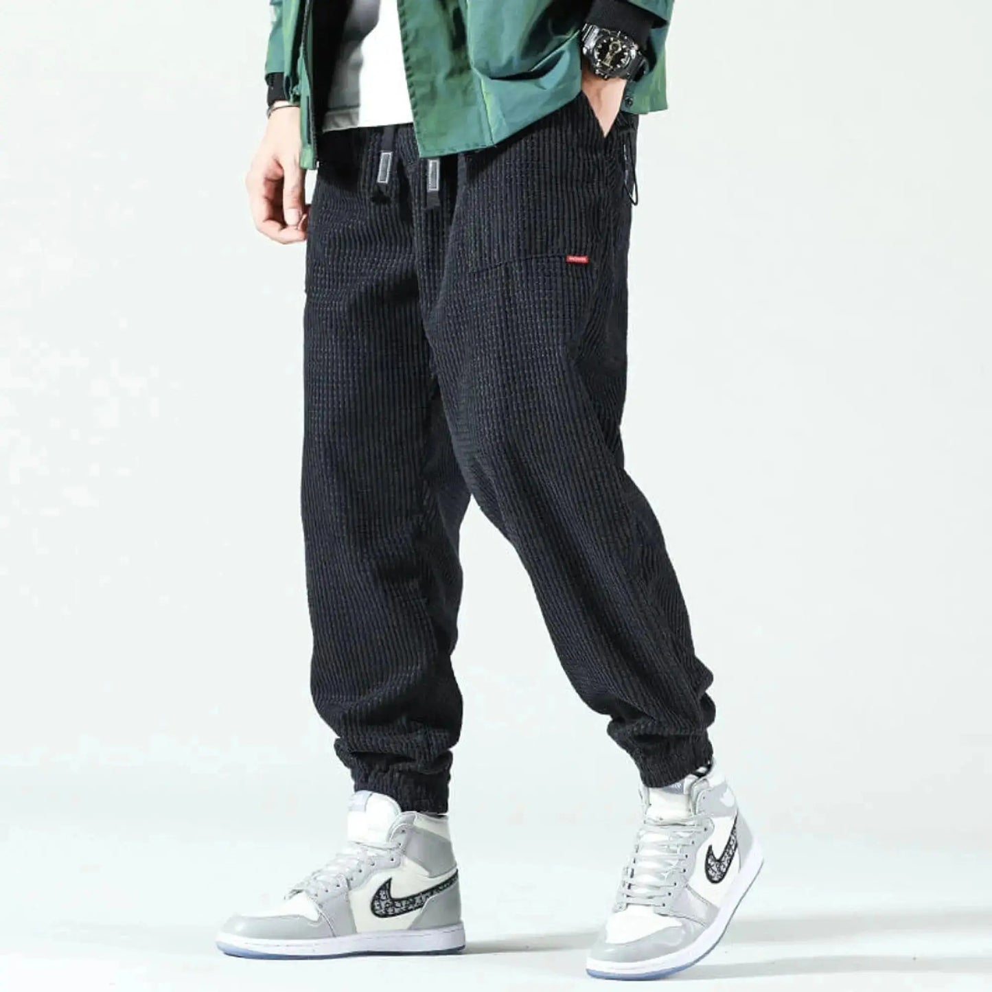 Man wearing black corduroy joggers with elastic cuffs, standing sideways, paired with gray sneakers