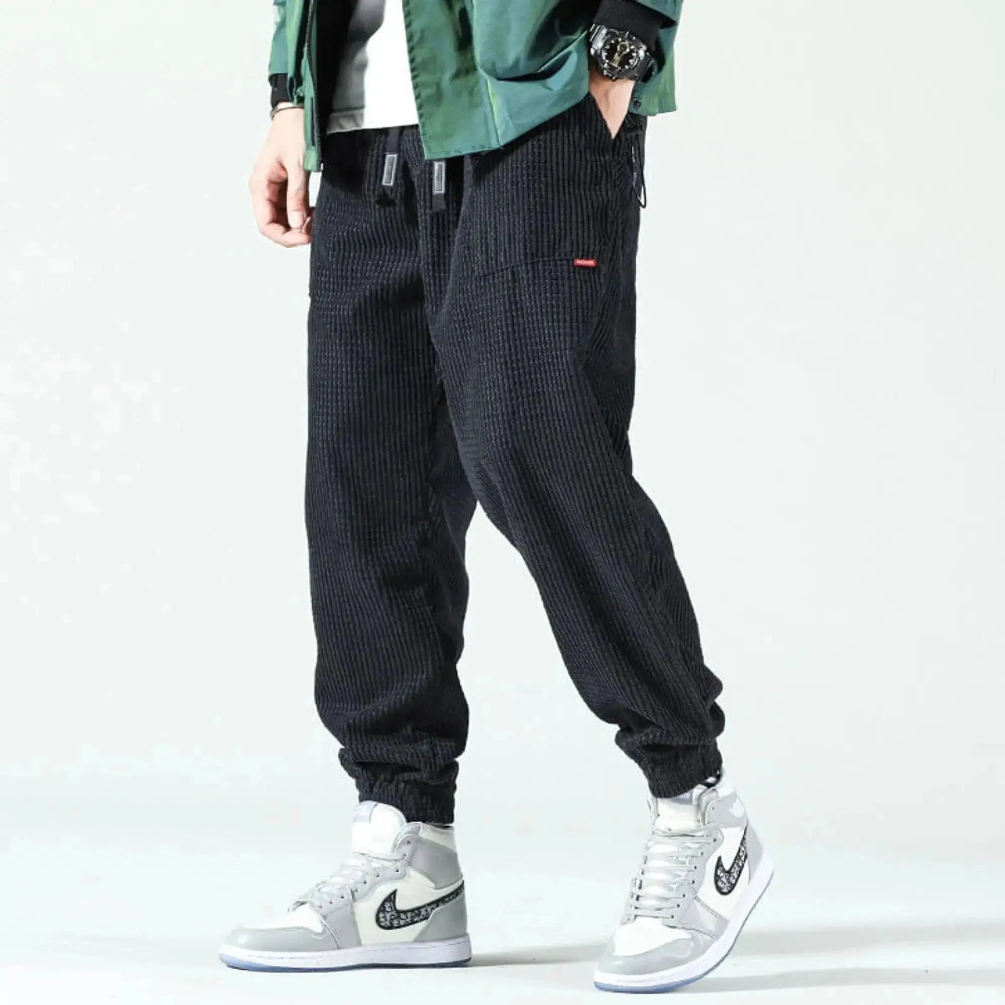 Man wearing black corduroy joggers with elastic cuffs, standing sideways, paired with gray sneakers