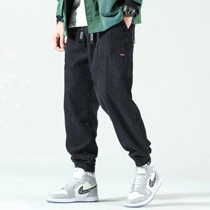 Man wearing black corduroy joggers with elastic cuffs, standing sideways, paired with gray sneakers