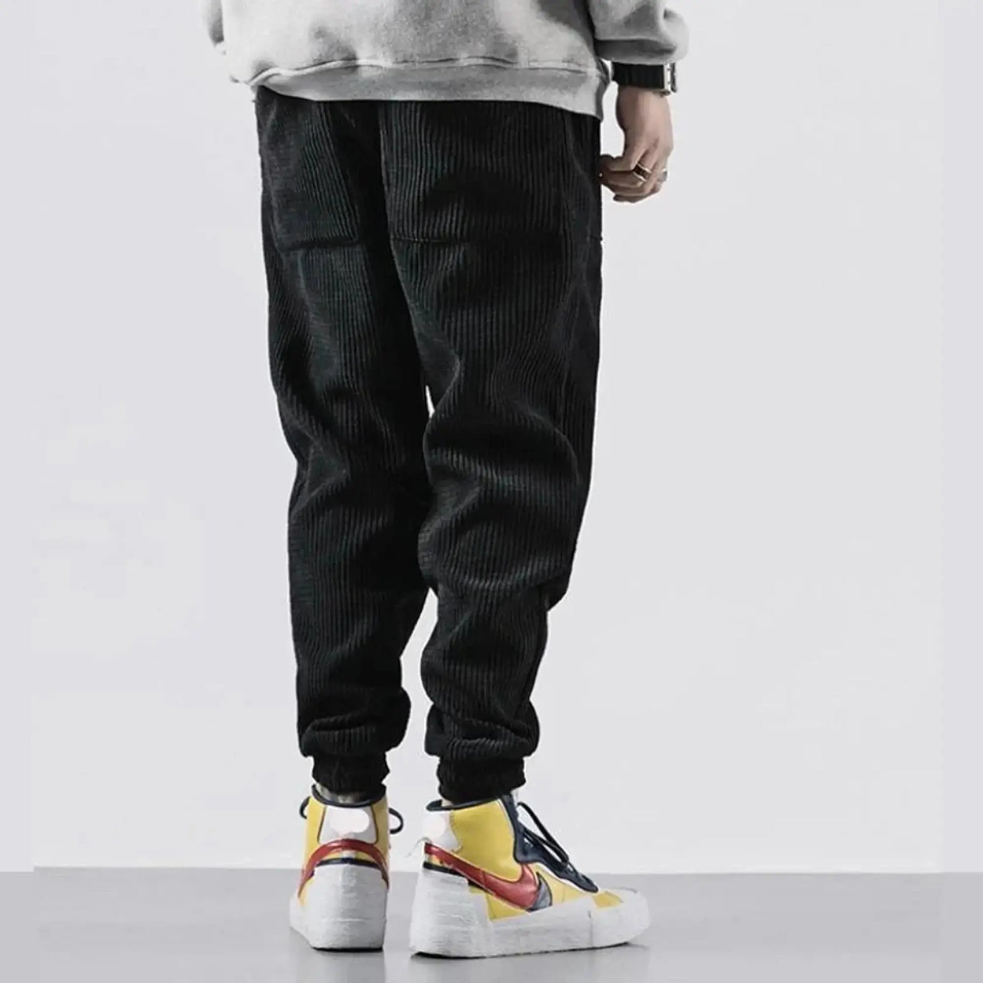 Man wearing black corduroy joggers, standing sideways, showing elastic cuffs and large pockets