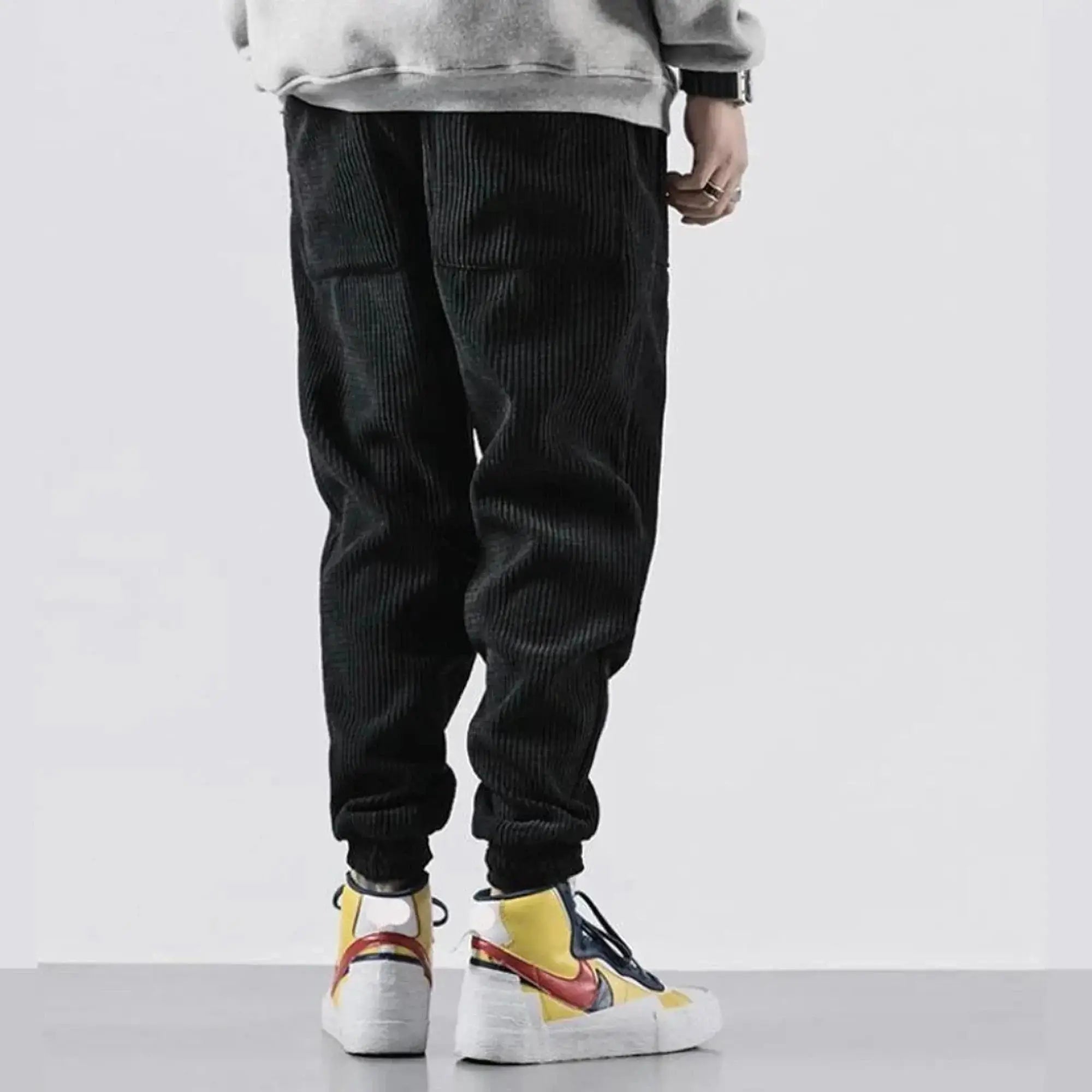 Man wearing black corduroy joggers, standing sideways, showing elastic cuffs and large pockets