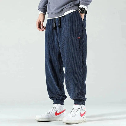 Man wearing navy corduroy joggers with drawstring, standing sideways, hands in pockets, white sneakers