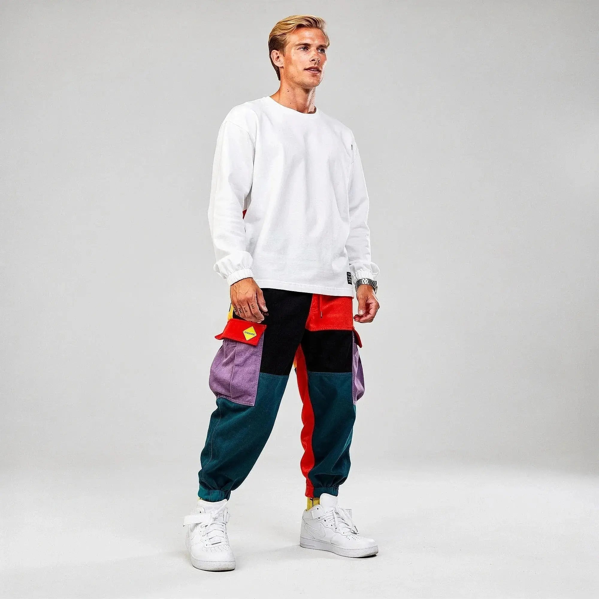 Man wearing colorful cargo joggers with purple, red, and teal patches, white sweatshirt, and sneakers