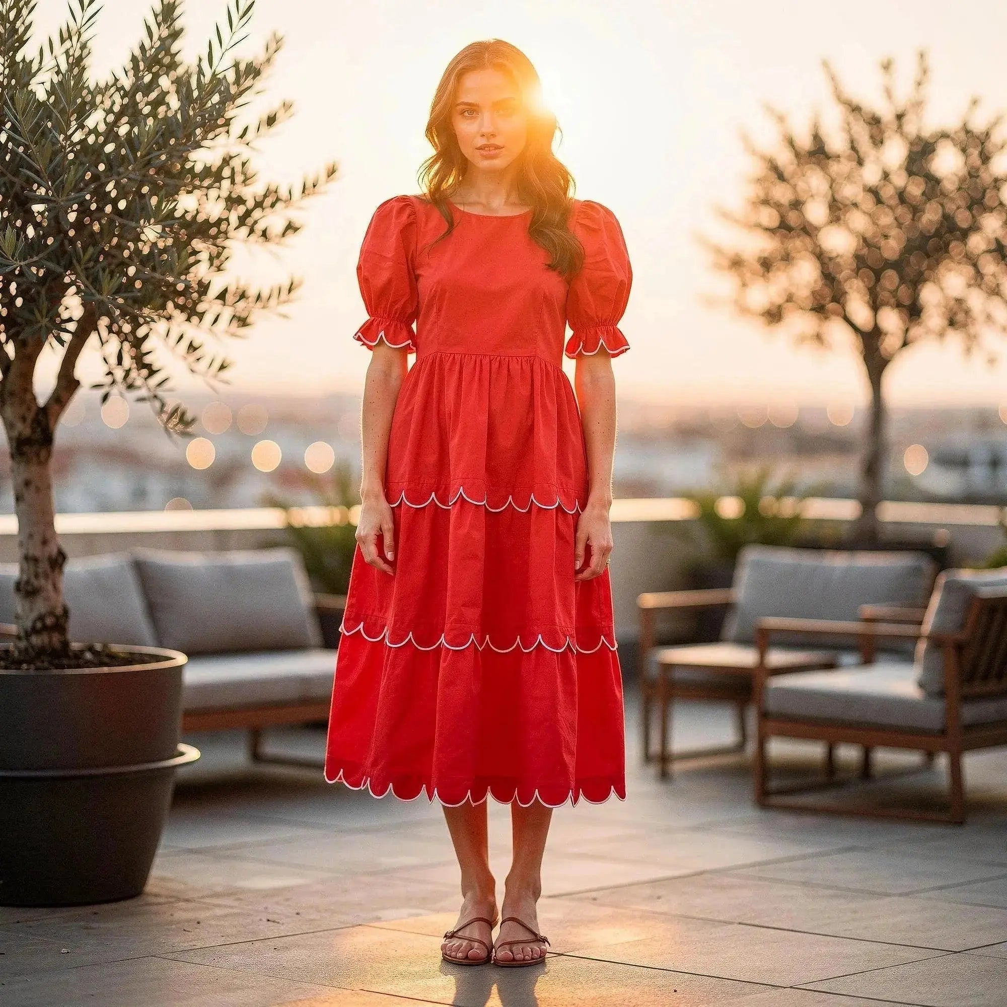 Woman wearing red A line midi dress with puff sleeves and scalloped hem, standing on rooftop patio