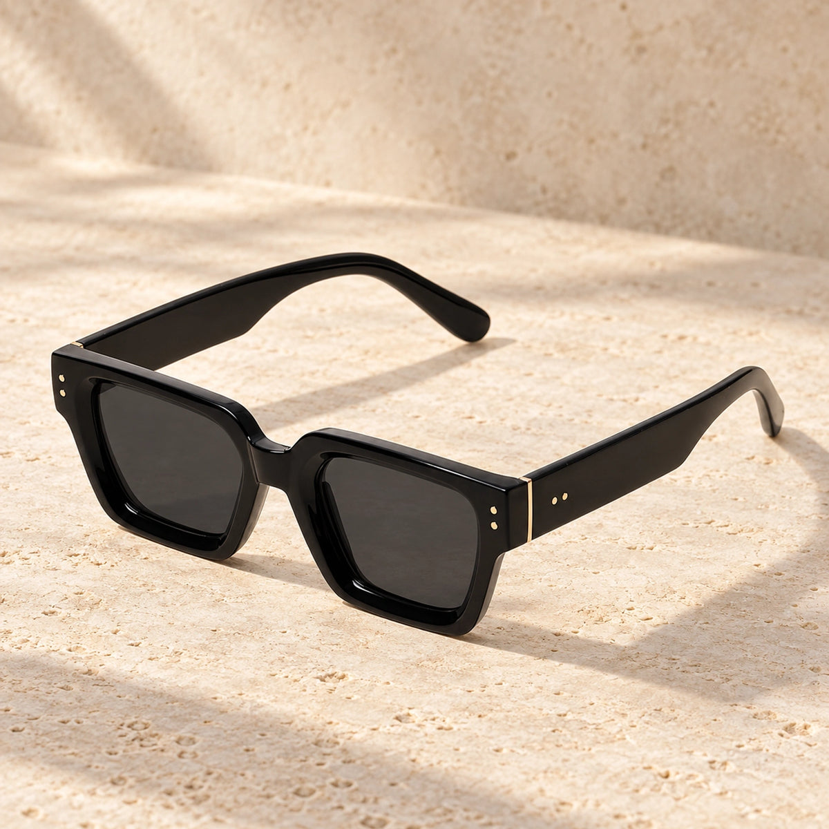 Rivet Black Charcoal sunglasses, complete pair on a warm neutral stone surface. — view 13