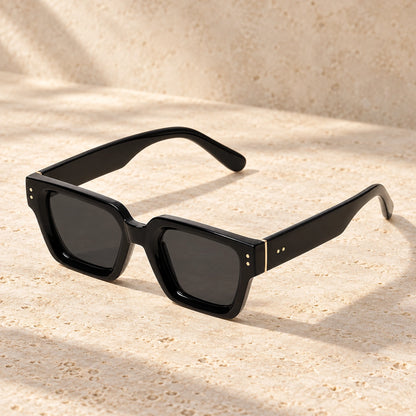 Rivet Black Charcoal sunglasses, complete pair on a warm neutral stone surface. — view 13